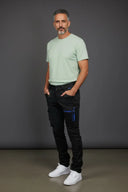 Frontansicht, nach vorne links ausgerichtetes männliches Modell  in der Eskotomic Winterreithose für Islandpferdereiter vor grauem Hintergrund, an der Hose sind zwei Taschen mit wasserdichtem blauem Reißverschlüssen und zwei weiteren Taschen für die Hände, optimal für Reiten und Arbeiten, schwarzer Softshellstoff.