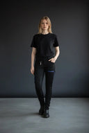 Frontansicht eines in der Bewegung stehenden Modells, dass die Winterreithose Damen von Eskotomic trägt, vor dunklem Hintergrund, die Reißverschlüsse sind aus wasserdichtem Material in blau. Man erkennt gut den Grippbesatz und den Softshellstoff, die Reithose ist eine Mischung aus Jodpurhose und Stiefelhose, perfekt zum Arbeiten und Reiter.